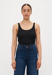 Svart scoop-neck tank topp laget av glatt stoff, kombinert med høyhalsede blå denimjeans med knappelukking og klassisk søm.