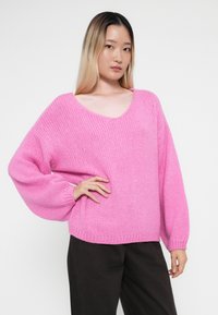 Maglione rosa lavorato a maglia con scollo a V, spalle scese e maniche lunghe. Tessuto texturizzato e polsini a costine con una vestibilità comoda.