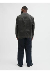 Tummanvihreä puuvillacollari, jossa on näkyvät ompeleet. Siinä on kaulus ja napitusyksityiskohdat. Yhdistetty löysiin tummiin housuihin ja mustiin kenkiin.