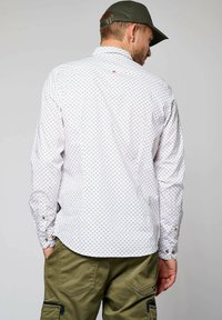 Witte lange mouwen shirt met een geometrisch patroon in blauw en rood, voorzien van knoopmanchetten en een gebogen zoom, gecombineerd met groene cargobroek.