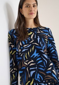 Haut à manches longues en bleu marine foncé avec un motif botanique vif en bleu, jaune, brun et beige. Tissu lisse avec un col rond.