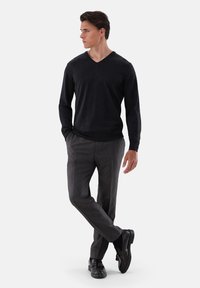 Schwarzer V-Ausschnitt-Pullover, lange Ärmel; graue Karohose, schmal geschnitten; schwarze Loafers mit Quasten. Neutraler Hintergrund.