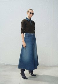 Denim rok met een A-lijnvorm, gecombineerd met een donker trui met een contrasterende blauwe kraag, geaccentueerd met ronde zwarte zonnebrillen.