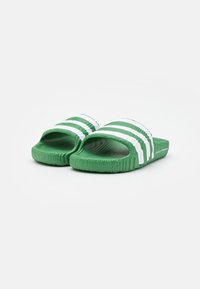 Gröna slide-sandaler med vita ränder, tillverkade av texturerad gummi. Har en öppen tådesign och en räfflad sula för bättre grepp.