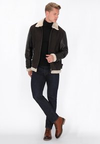 Jachetă bomber din piele maro, cu guler și mansete din blană sintetică crem, având detalii cu nervuri la umeri, buzunare cu fermoar și un design ajustat.