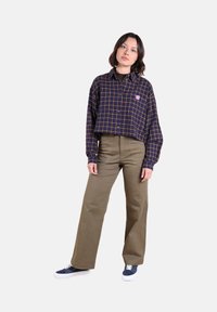 Chemise à carreaux bleu marine avec des lignes jaunes, à boutons sur le devant, associée à un pantalons taille haute vert olive et des baskets bleu marine.