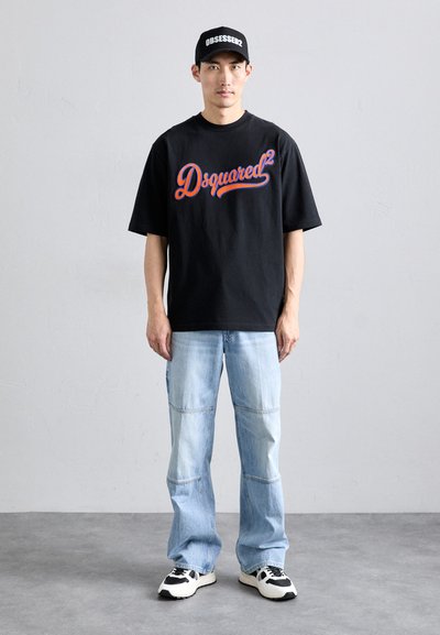 T-shirt nera in cotone con logo "Dsquared2" rosso e blu, abbinata a jeans in denim azzurro chiaro con cuciture a pannello e sneakers. Cappellino nero con testo "OBSESSED".