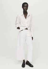 White button-up shirt, loose-fit white trousers, and black loafers. Smooth fabric with a clean design and wide pant legs.