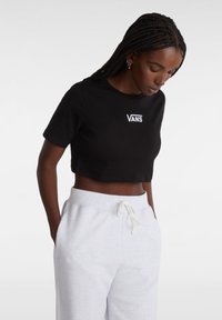 Sort cropped T-shirt med hvid "VANS" logo på brystet. Blødt bomuldsstof, korte ærmer, rund halsudskæring. Kombineret med grå sweatpants.