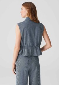 Top senza maniche a righe blu navy e bianche con orlo a peplum e colletto, realizzato in tessuto leggero. La vista posteriore mostra un design aderente.