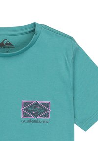 Tyrkysové bavlněné tričko s kulatým výstřihem. Na levém prsu má grafické logo v černé a růžové barvě. Krátké rukávy, volný střih.