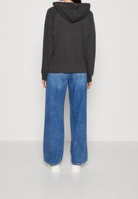 Sweat à capuche gris charbon avec une poche à l'arrière, associé à un jean denim bleu clair ample. Des chaussures blanches complètent le look.