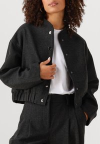 Zwarte gecropte jas van textuurstof, met een drukknoopsluiting, ronde halslijn en een gerimpelde zoom voor een aansluitende look.