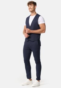 Chaleco azul marino con un corte ajustado y escote en V pronunciado, combinado con pantalones a juego; tejido texturizado; estilizado con zapatillas blancas.