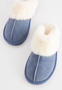 Sinised seemisnahast sussid kreemja kunstkarvaga mansetiga. Ümar varbakuju, õmblustega detailid ja tekstureeritud tallaosa haardumise tagamiseks.