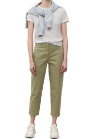 Licht olijfgroene broek met een rechte snit, gecombineerd met een wit t-shirt en een lichtblauwe sweatshirt over de schouders. Witte sneakers.