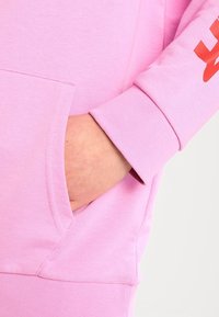 Felpa rosa con tasca frontale, polsini a costine e stampa grafica rossa sulla manica. Tessuto morbido con una texture liscia.