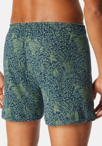 Pantalones cortos para hombre en azul oscuro con un patrón floral y de hojas en verde. Cuentan con una cinturilla elástica y un ajuste suelto y cómodo.