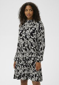 Must kleit valge lillelise paisleimustriga, pikad varrukad, kõrge kaelus ja kihiline seeliku disain, tehtud kerge ja tekstuurse kangaga.