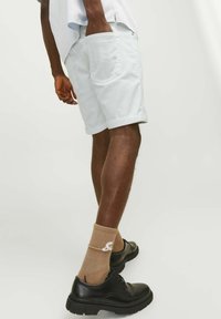 Pantalones cortos de algodón azul claro con dobladillos enrollados, combinados con zapatos de vestir negros y calcetines de canalé color beige con detalle de logo blanco.