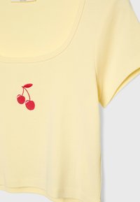Gul bomullskort top med rund halsringning och korta ärmar, prydd med röda broderade körsbär på vänstra sidan.