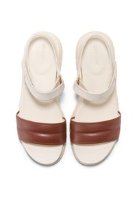 Correas de cuero marrón sobre una base beige con una correa para el tobillo texturizada. La suela gruesa proporciona amortiguación y soporte. Diseñadas para la comodidad y el estilo.