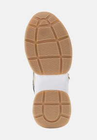 Gummisohle in Hellbraun mit strukturiertem Grip-Muster. Weiße Zwischensohle mit geprägtem "GUESS"-Logo. Leicht gebogene Form.