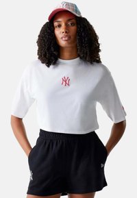 Witte cropped t-shirt met rood geborduurd "NY" logo, gecombineerd met zwarte shorts met een elastische tailleband en zijzakken.