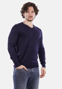 Maglione blu navy a V, realizzato in tessuto lavorato a maglia, con maniche lunghe e polsini a coste. Abbinato a jeans blu chiaro.