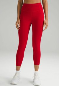 Leggings active roșii, cu talie înaltă, realizate dintr-un material elastic cu o textură fină, având buzunare laterale și cusături detaliate.