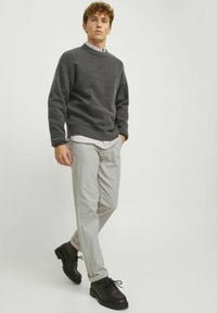 Grauer Strickpullover, hellgraue Hose und schwarze Schuhe. Der Pullover hat einen Rundhalsausschnitt und gerippte Bündchen; die Hose ist geradlinig geschnitten.