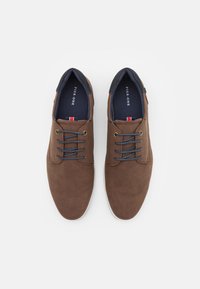 Zapatos sintéticos marrones con textura suave, puntera redonda, cordones grises y diseño minimalista. Presentan un cuello azul marino y un logo en la plantilla.