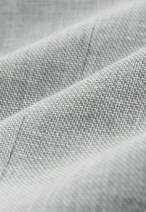 Šviesiai pilka tekstūruoto audinio su smulkiais raštais ir minkštais, lygiais paviršiais. Artimas vaizdas, rodantis subtilias siūlių detales.