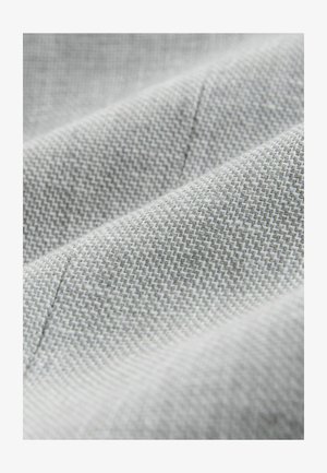 Hellgrauer Stoff mit einer strukturierten Webart, der feine Muster und weiche, glatte Oberflächen aufweist. Nahaufnahme mit dezenten Nähdetails.