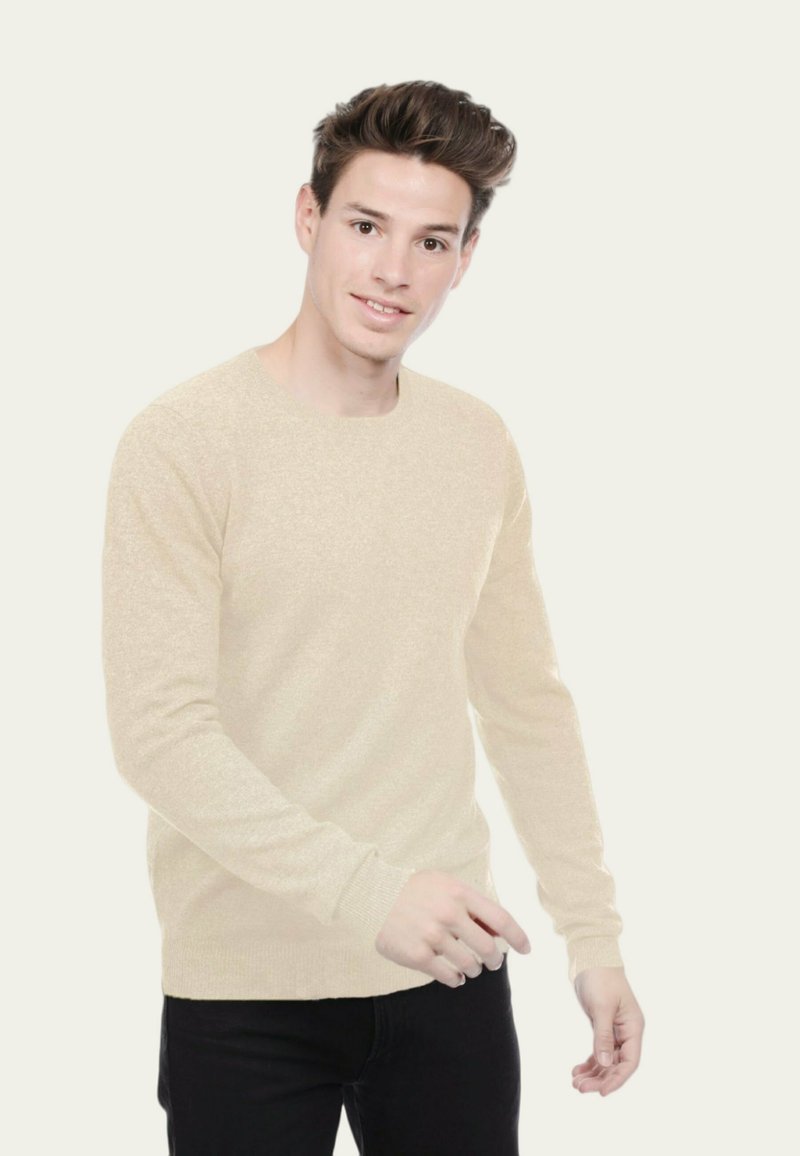 Pull long à manches longues beige clair avec un col rond et une surface texturée, associé à un pantalon noir. Le pull présente des poignets et un ourlet ajustés.