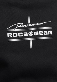 Tela negra con un destacado logo blanco que dice "Rocawear", acentuado por líneas horizontales por encima y por debajo.