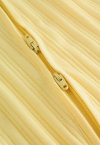 Gelbes geripptes Gewebe mit einem zentralen gelben Reißverschluss, der zwei Schieber nahe beieinander aufweist.