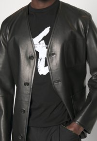 Black leather jacket with a relaxed fit, six buttons, and a chest pocket, layered over a black t-shirt featuring white graphic text.