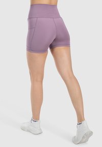 Paarse high-waisted shorts met een gladde textuur, voorzien van zijzakken en een strak ontwerp, gecombineerd met witte sportschoenen.