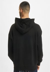 Felpa nera con una texture morbida, dotata di un ampio cappuccio, vestibilità rilassata e orlo a costine. Nessun motivo visibile o dettagli in metallo.