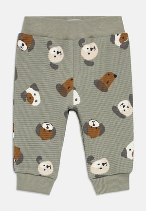 Pantalon pour bébé en tissu gaufré vert avec un motif de têtes de chiens marron, blanc et gris, taille et poignets côtelés.