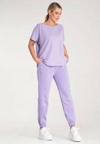 Fioletowy zestaw odzieży domowej składający się z luźnej bluzki z krótkim rękawem oraz dopasowanych spodni dresowych z elastycznymi mankietami. Wykonany z miękkiego, gładkiego materiału. Białe sneakersy.