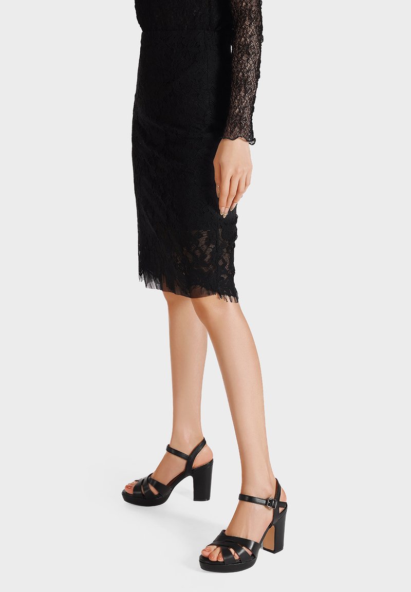 Sandali con plateau neri, dotati di ampie fasce incrociate, un tacco alto massiccio e una cinghia alla caviglia. Il design presenta una texture in pelle liscia.