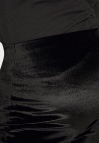 Saia de veludo preto com uma textura suave e brilhante e um design justo. O tecido tem um leve brilho, criando uma aparência rica.