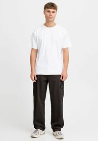 Weißes Baumwoll-T-Shirt, Rundhalsausschnitt, kurze Ärmel, kombiniert mit schwarzen Cargo-Hosen mit seitlichen Taschen. Schuhe in Hellgrau mit Akzenten.
