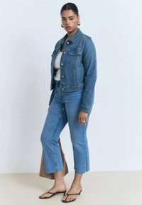 Blå denimjakke med to frontlommer, parret med højmidte blå jeans med en kortet kant. Brun skuldertaske og sandaler.