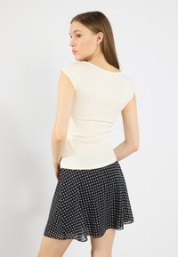 Camiseta de canalé crema con mangas cortas combinada con una falda negra de lunares. La falda es ligera y se despliega, añadiendo movimiento.