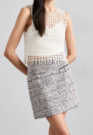 Vrouw draagt een mouwloos wit gehaakt pareltjes topje en een hoog-getailleerde, gestructureerde zwart-witte minirok met knoopzakken.