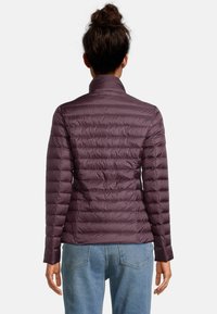 Fialová nadýchaná bunda s vysokým límcem, prošívanou texturou a dlouhými rukávy. Nahoře nošena přes džíny se dvěma zadními kapsami ve světlém odstínu.