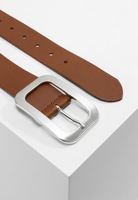 Ceinture en cuir texturé marron avec une boucle en métal argenté rectangulaire. Comprend plusieurs trous pour un ajustement de taille.